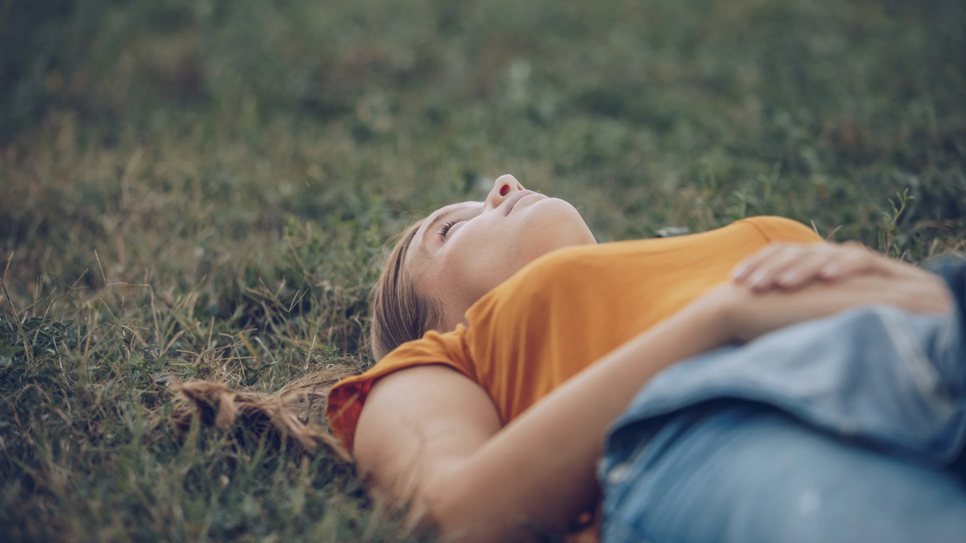 Frau liegt im Gras und schaut in den Himmel